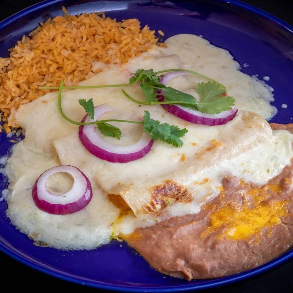 El Tenampa's enchiladas with white sauce, rice, refried beans, red onion, and cilantro on a blue plate.