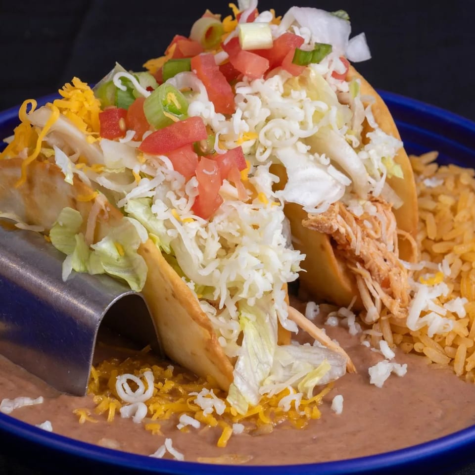 Two chicken tacos with lettuce, tomatoes, cheese, and green onions, served with rice and beans.