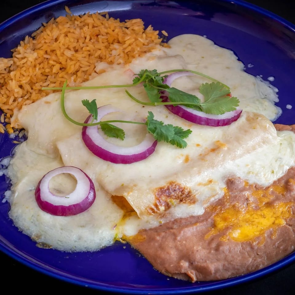 El Tenampa's enchiladas with white sauce, rice, refried beans, red onion, and cilantro on a blue plate.
